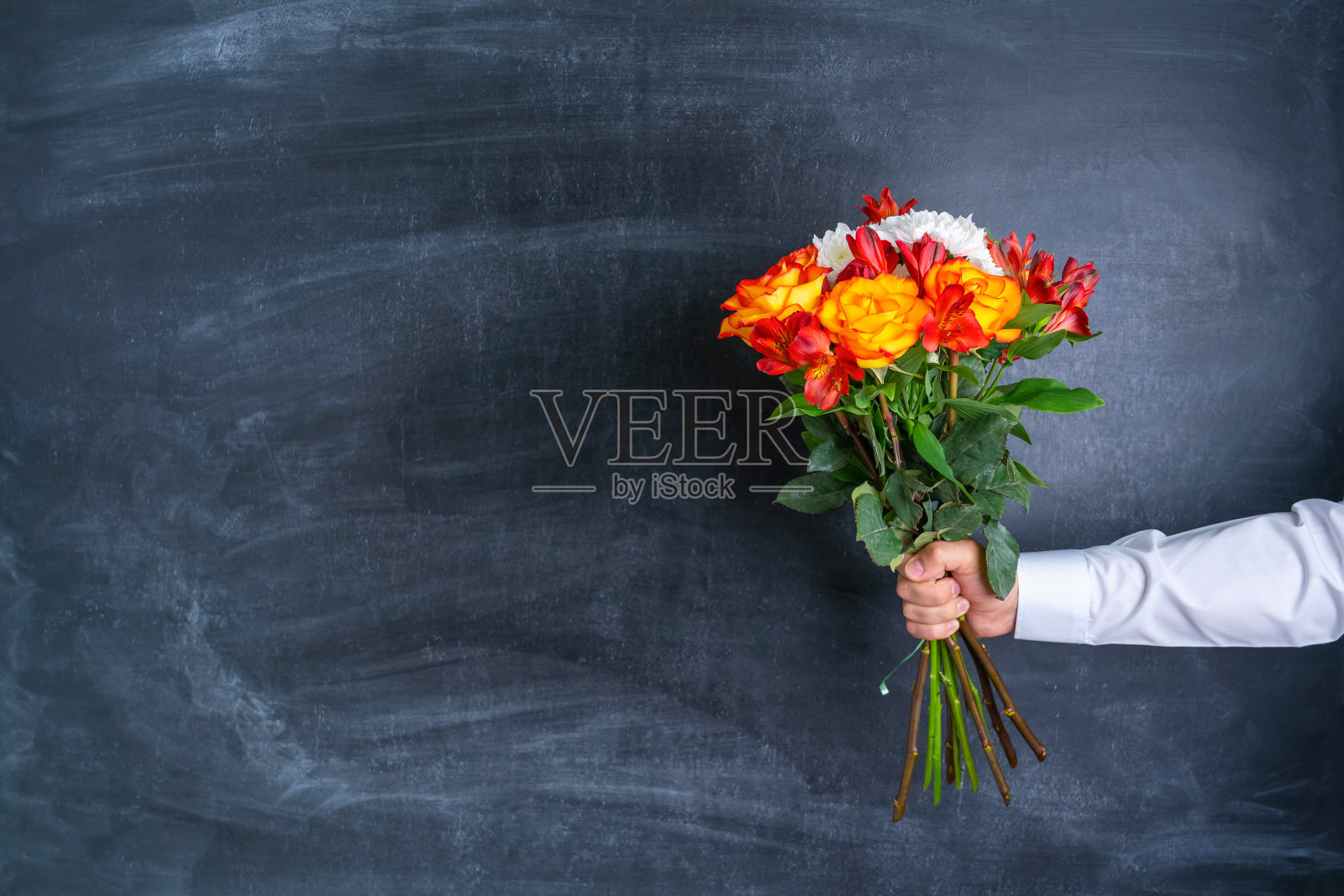 在黑板的背景上，一个男人的手拿着一束鲜花。照片摄影图片