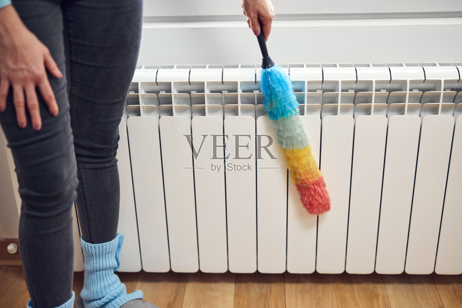 一位妇女拿着一根灰尘棒在清洁家里的暖气暖气片。照片摄影图片