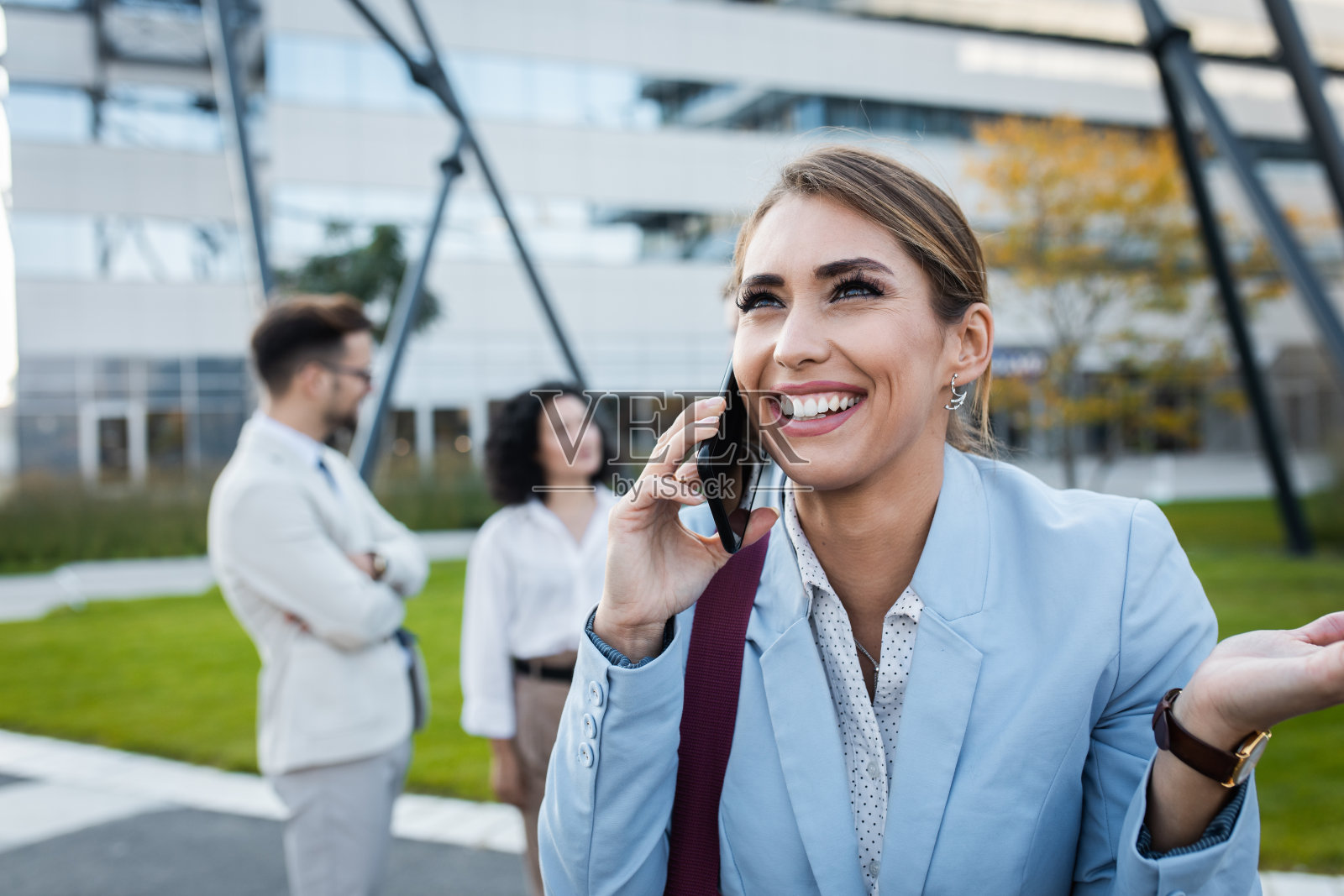 微笑着站在现代办公大楼前使用智能手机的女商人肖像。照片摄影图片