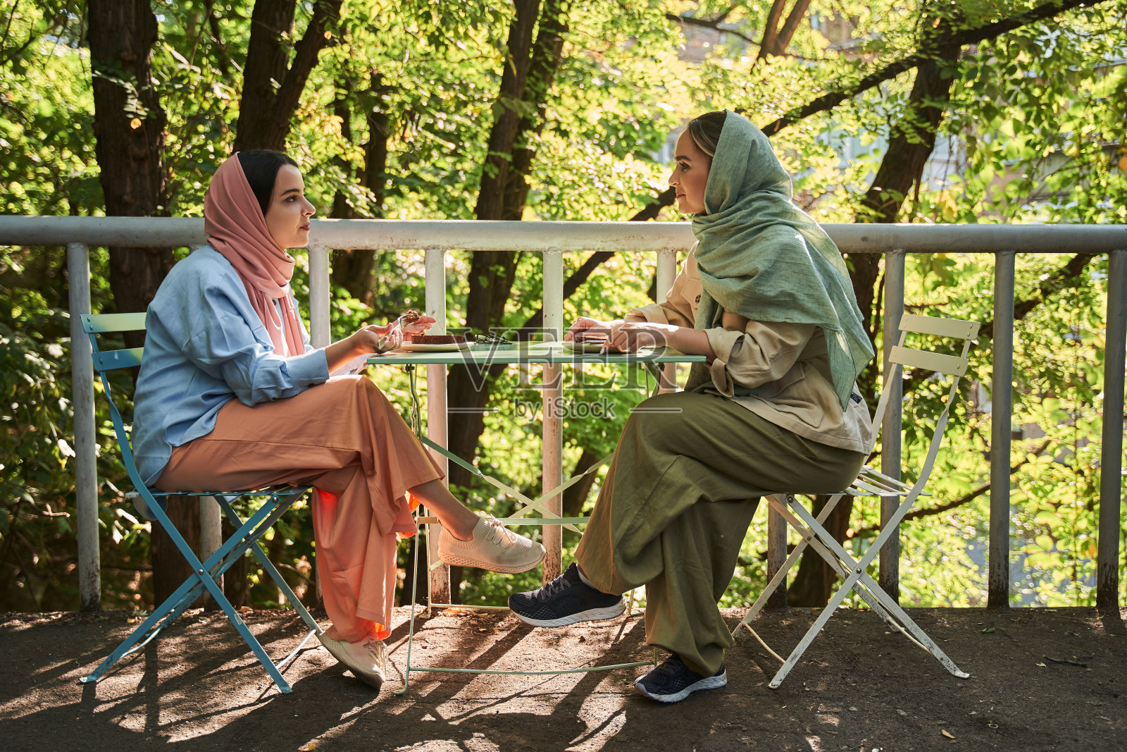 一个穆斯林妇女戴着头巾，坐在街边的咖啡馆里吃着饭，看着她最好的朋友照片摄影图片