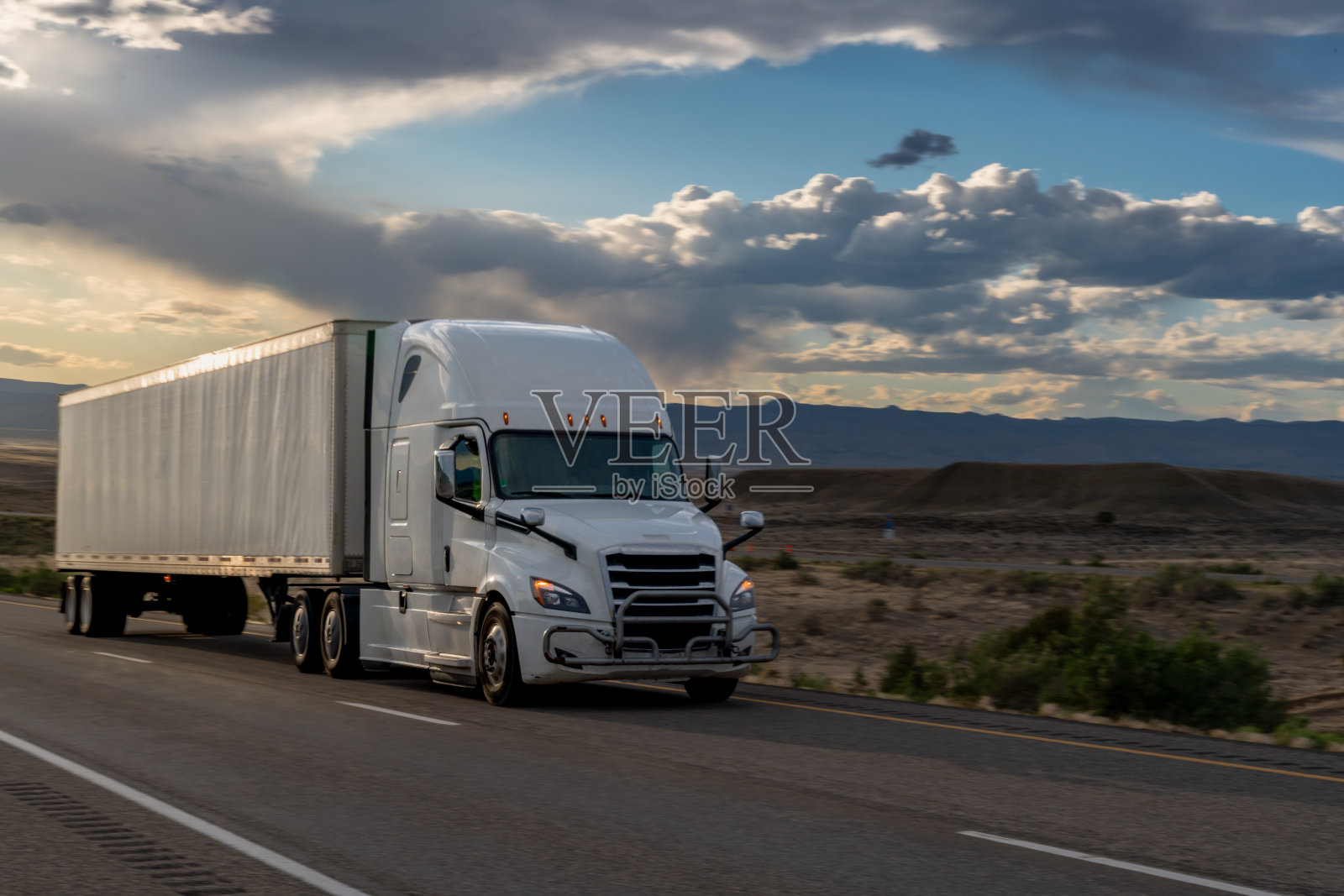 黄昏时分，在戏剧性的天空下，白色半卡车在犹他州沙漠的高速公路上超速行驶照片摄影图片