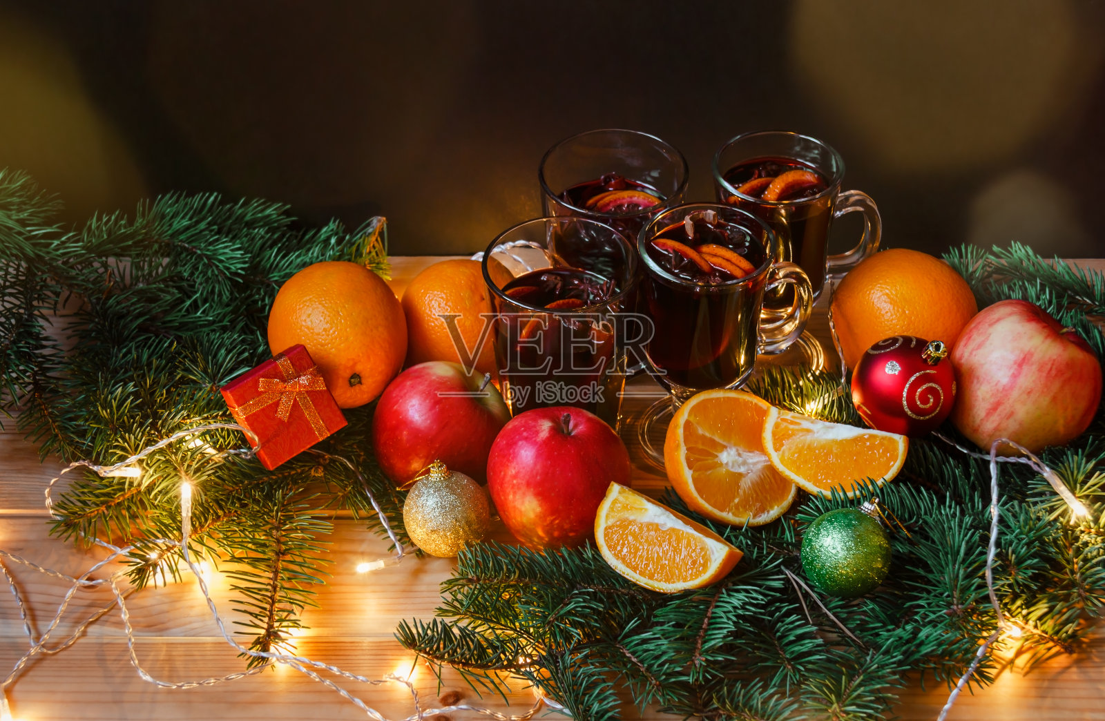 一杯热红酒，苹果，桔子，圣诞球，礼物，冷杉枝和发光的圣诞灯。有选择性的重点。照片摄影图片