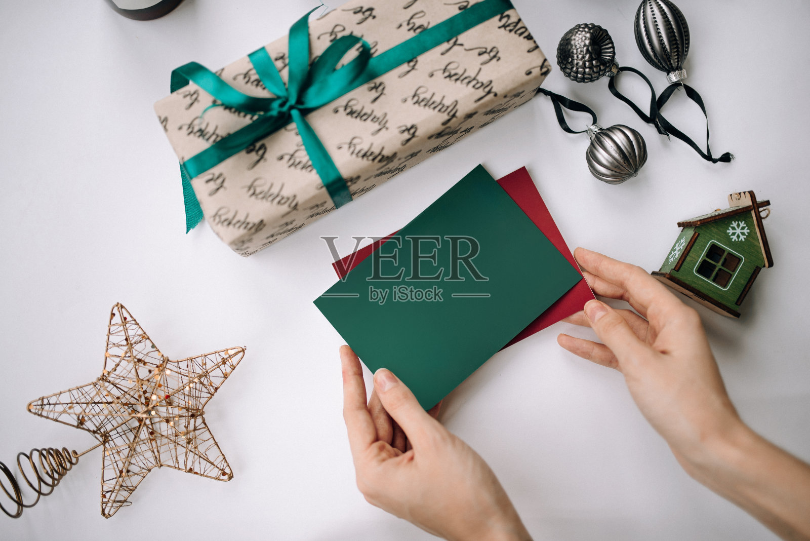 手握空白的圣诞卡片在白色的桌子背景与圣诞包装的礼物和装饰照片摄影图片