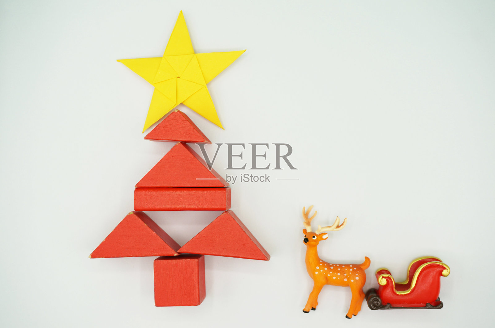 圣诞五角星在黄色的折纸上，红色的方块做成概念圣诞树，麋鹿用红色的雪橇。白色的背景材料在圣诞节的精神。照片摄影图片