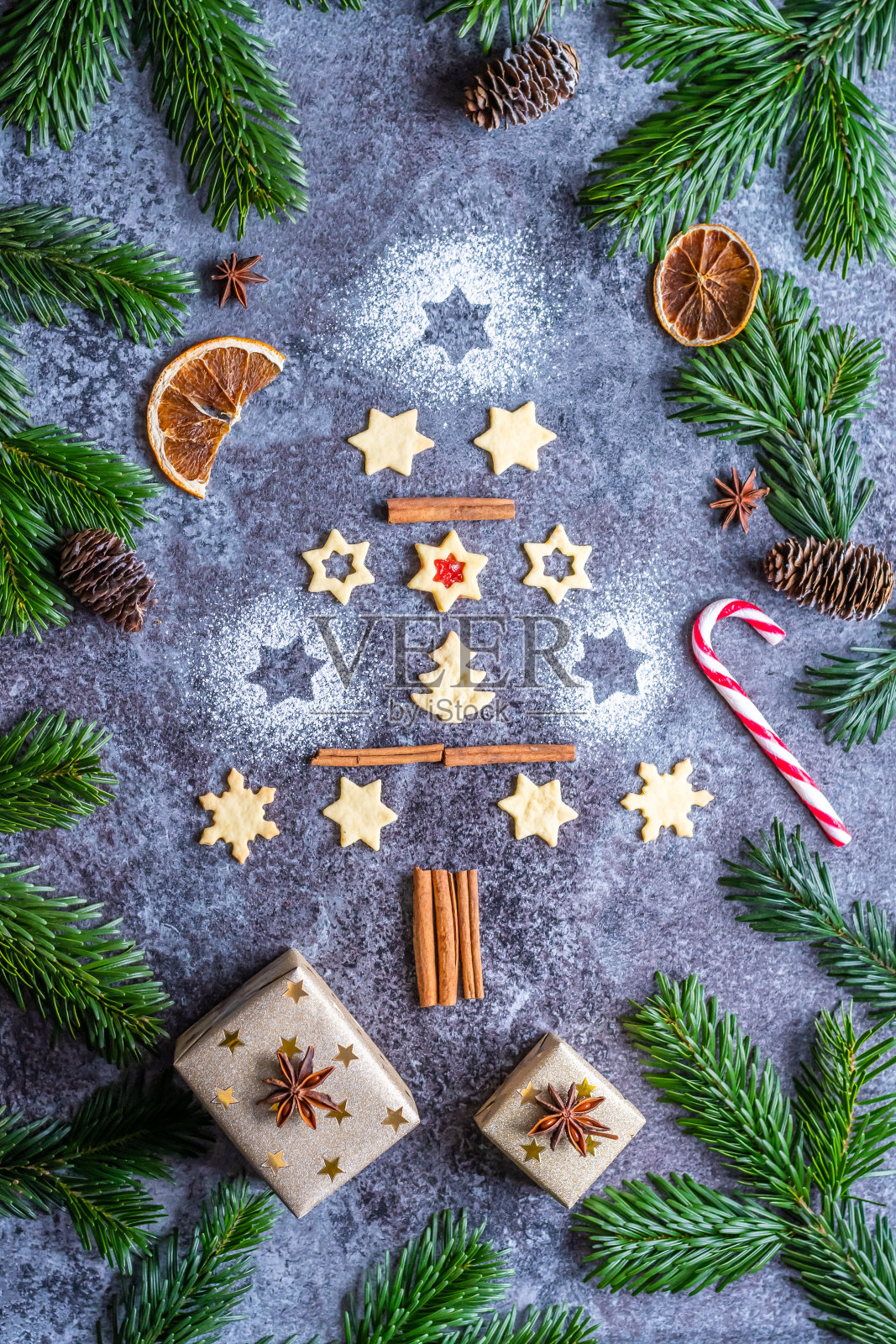 灰色的桌子上摆放着一棵圣诞树，旁边放着松果和树枝。冬天和圣诞节的装饰品，肉桂，糖和八角茴香。照片摄影图片