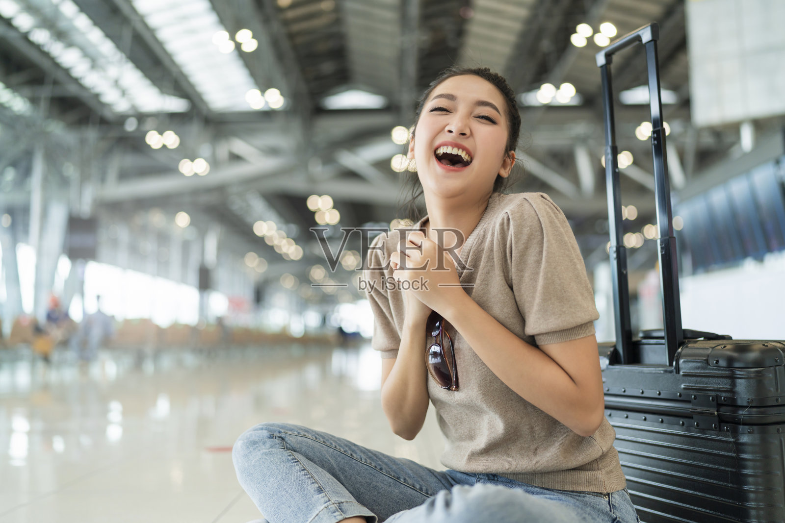 亚洲女性旅行者穿着休闲的布料挥手微笑，坐在机场航站楼的地板上放松，带着行李安全旅行的概念照片摄影图片