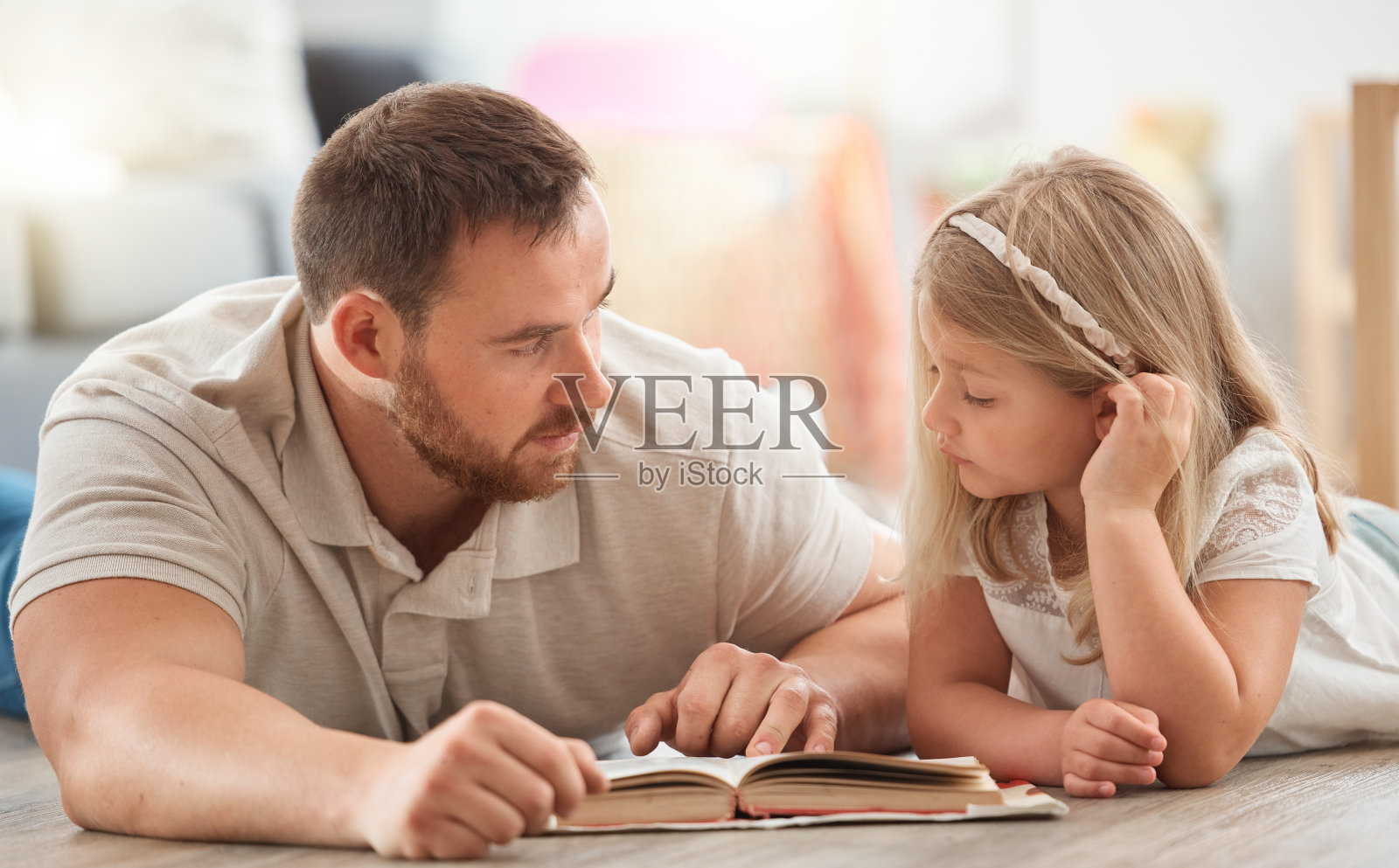 这张照片拍摄的是一对年轻的父亲和女儿在家里一起看书照片摄影图片