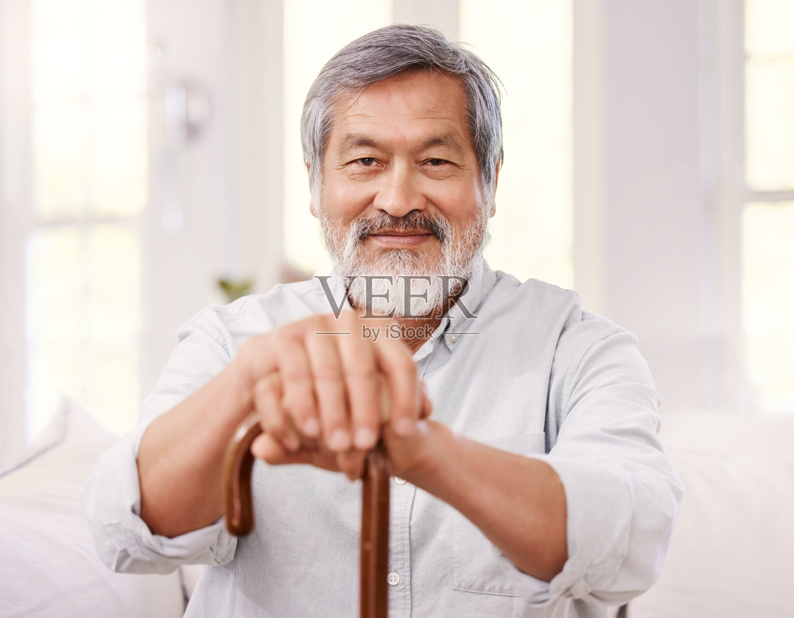 一个老人坐在家里，拄着一根木拐杖照片摄影图片