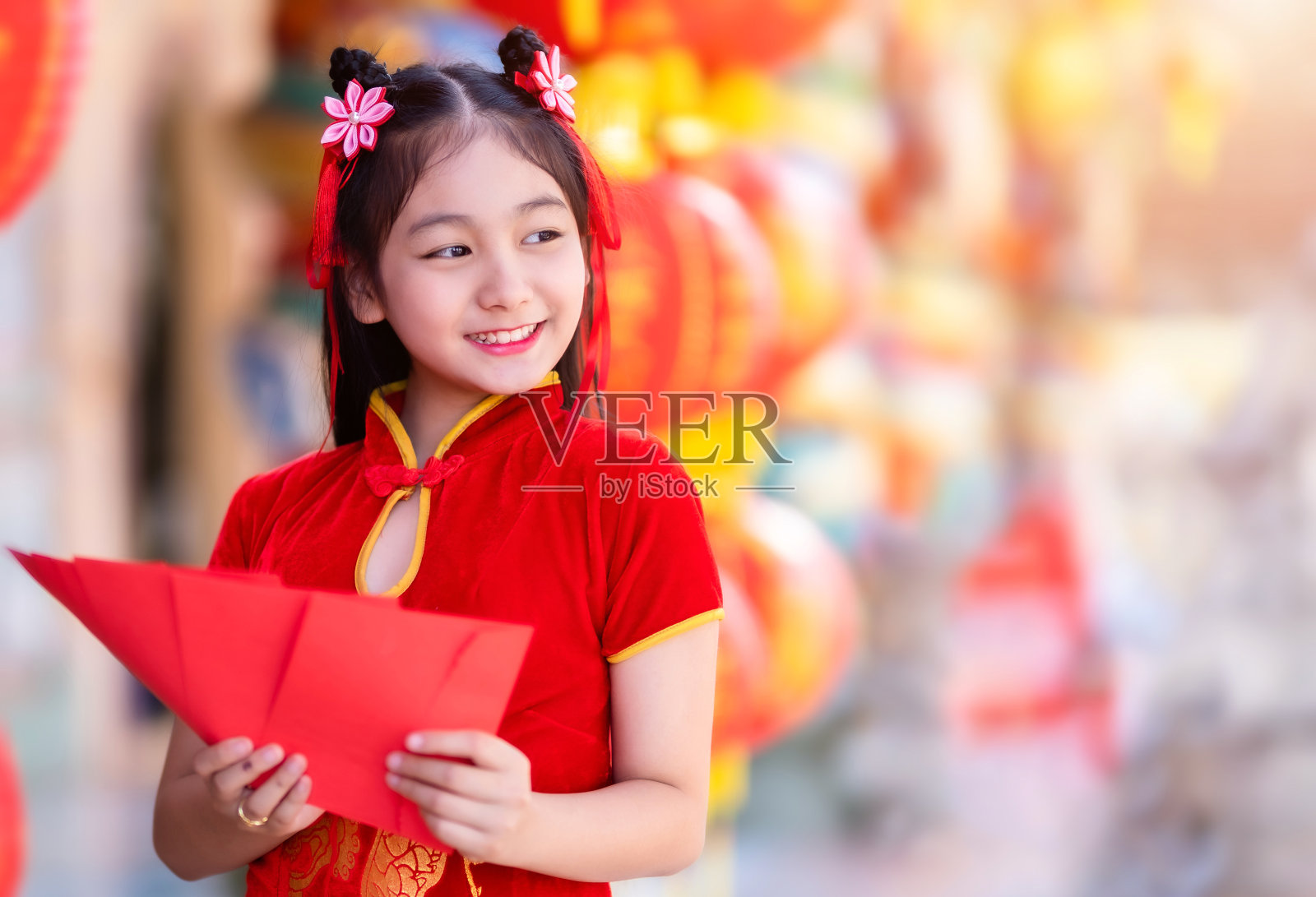 亚洲女孩穿着红色的中国传统旗袍装饰，手里拿着红包，灯笼上写着中文的祝福是中国新年的财富祝福照片摄影图片