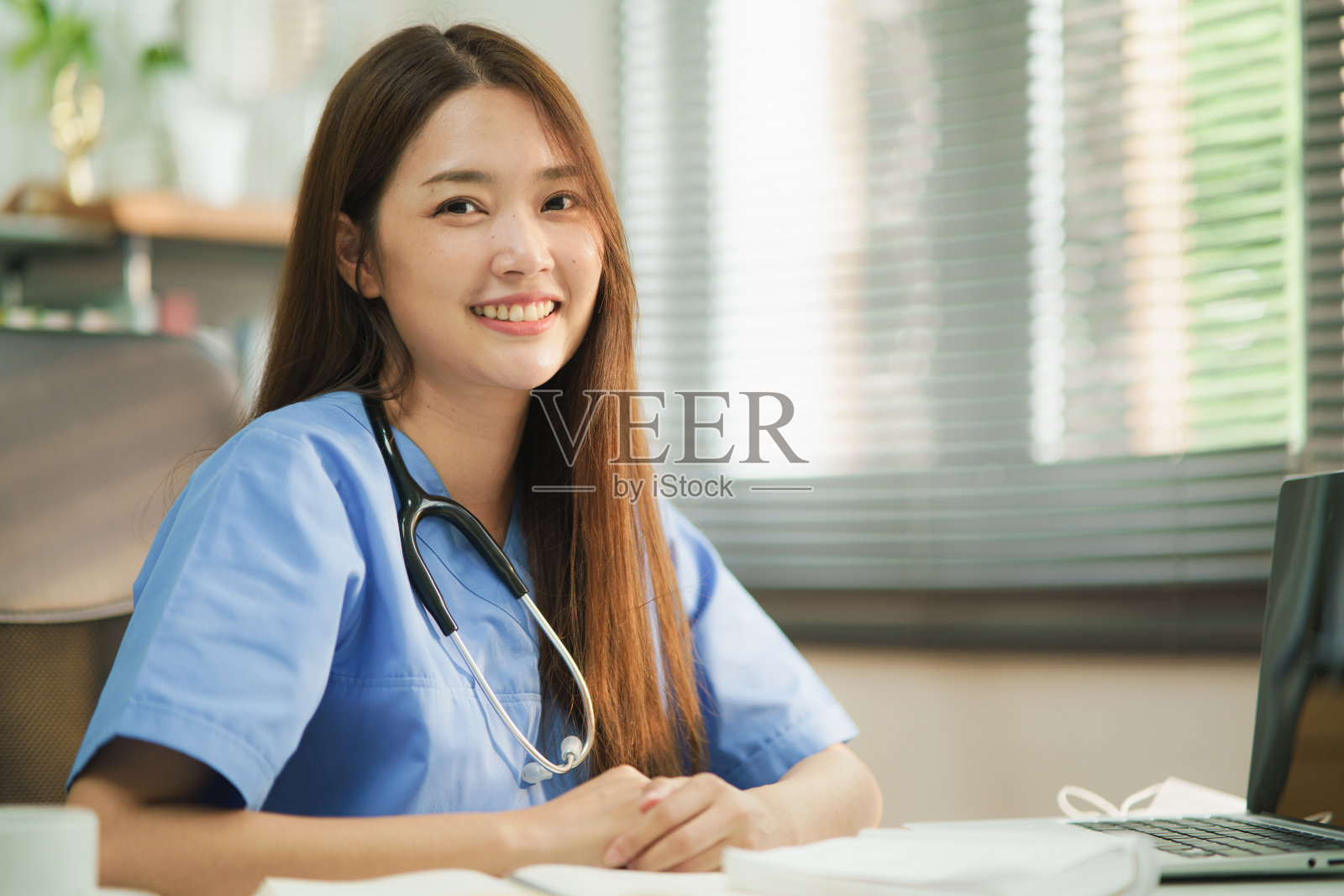 中等特写肖像亚洲女医生或护士与听诊器微笑对着相机，而坐在房间里。乐观的医务人员值班。幸福的医生肖像。照片摄影图片