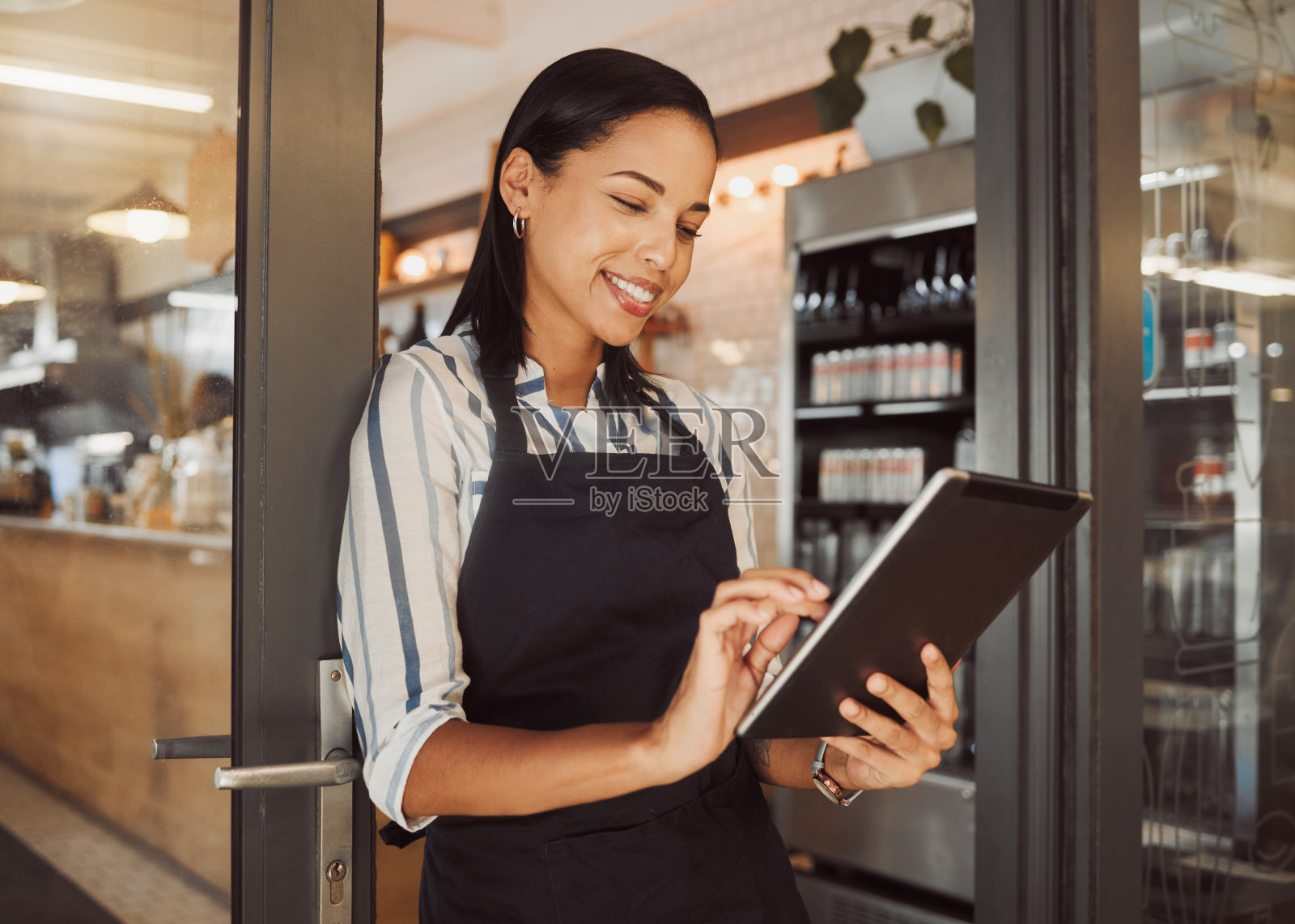 女商人在她的餐厅里使用电子平板电脑。咖啡店老板在她的商店入口处使用在线应用程序。自信的店主在她的杂货店里使用无线设备。照片摄影图片