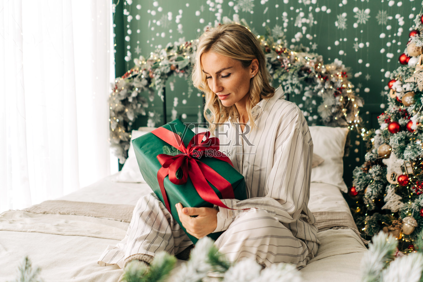 迷人的快乐女人坐在床上，在圣诞节的时候打开礼品盒照片摄影图片