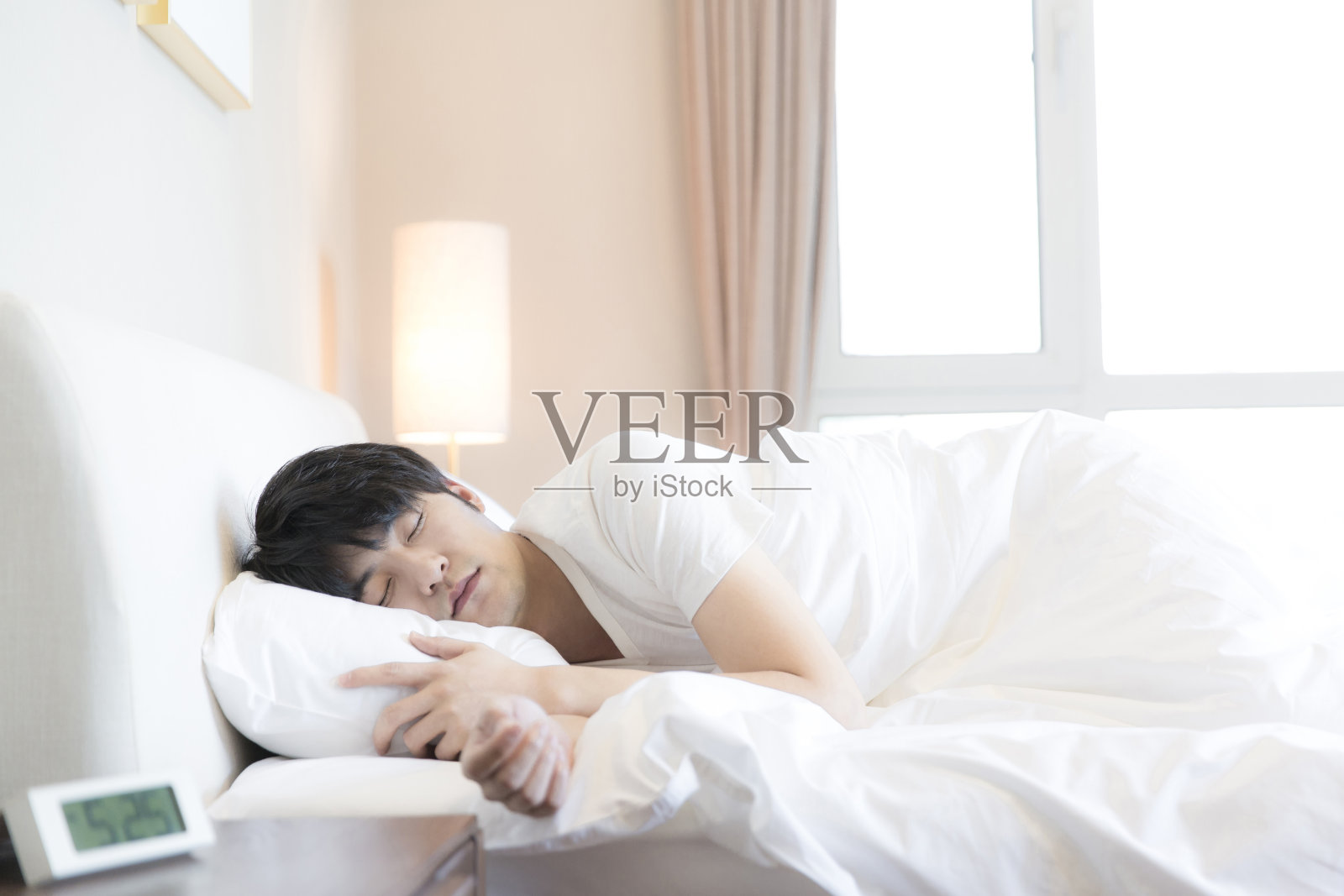 年轻的东亚人睡在他的一边在一个现代家庭卧室床-库存照片照片摄影图片