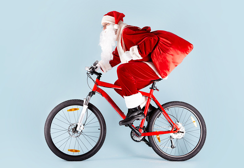 圣诞老人骑着自行车，把礼物装在红色的袋子里图片下载